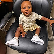Kyree is registered to the contest to win money with this photo: toddler, child, sitting, chair, office_chair, white_sneakers, shorts, tshirt, floor, indoor, person, happy, smiling, young_child, black_chair, casual_clothing, photography, cute, baby, leisure