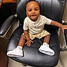 toddler, child, sitting, chair, office_chair, white_sneakers, shorts, tshirt, floor, indoor, person, happy, smiling, young_child, black_chair, casual_clothing, photography, cute, baby, leisure