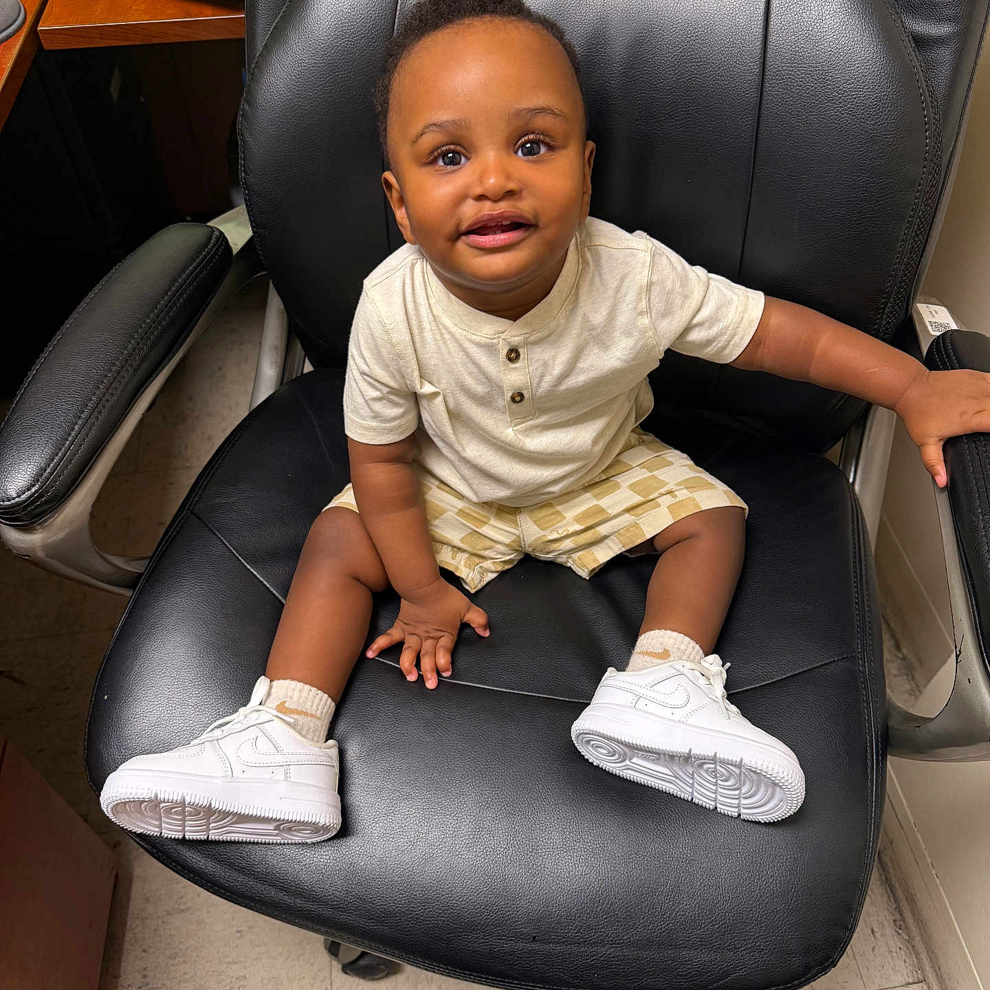 Kyree is registered to the contest to win money with this photo: toddler, child, sitting, chair, office_chair, white_sneakers, shorts, tshirt, floor, indoor, person, happy, smiling, young_child, black_chair, casual_clothing, photography, cute, baby, leisure