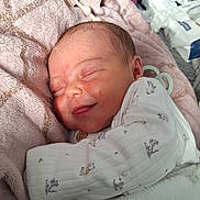 Athena is registered to the contest to win money with this photo: newborn, baby, sleeping, smiling, blanket, onesie, toy, wooden_toy, cozy, infant, cute, soft, comfort, sleep, face, hand, foot, fabric, child, person