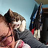 Izzy joined the competition — help win amazing prizes! cat, person, selfie, portrait, indoor, shoulder, gray_cat, white_paws, tabby, whiskers, ears, eyes, glasses, blanket, clothing, bedroom, blue_wall, closet, hanging_clothes, candid