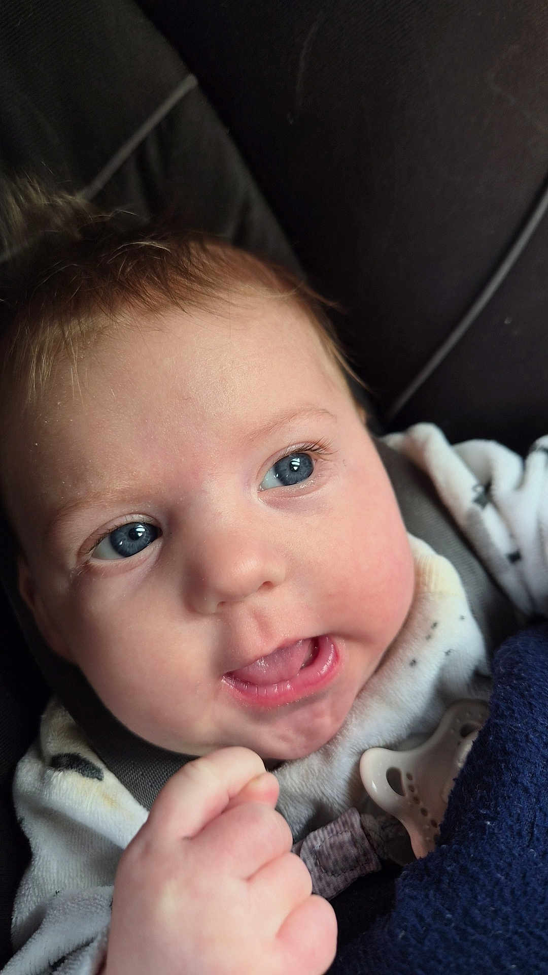 Luana a rejoint le concours — aidez-le/la à gagner de superbes lots ! baby, infant, face, blue_eyes, smile, mouth, tongue, hand, fist, pacifier, blanket, onesie, car_seat, cheek, eyelashes, skin, portrait, closeup, hair, cute