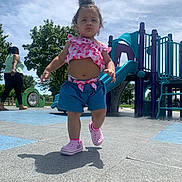 Damariana is registered to the contest to win money with this photo: child, toddler, playground, outdoor, park, walking, standing, smiling, curly_hair, pink_clothing, shorts, sneakers, slide, playground_equipment, trees, blue_sky, sunny, shadow, portrait, daylight