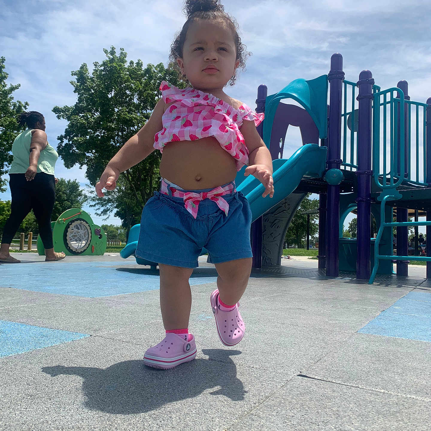 Damariana is registered to the contest to win money with this photo: child, toddler, playground, outdoor, park, walking, standing, smiling, curly_hair, pink_clothing, shorts, sneakers, slide, playground_equipment, trees, blue_sky, sunny, shadow, portrait, daylight
