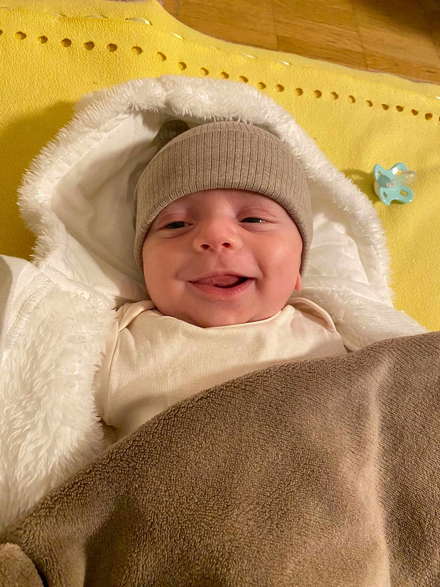 Emir Ali a rejoint le concours — aidez-le/la à gagner de superbes lots ! baby, smile, hat, blanket, pacifier, yellow_mat, white_jacket, cozy, infant, child, warm_clothing, indoor, cute, face, headwear, wrapped, happy, lying_down, soft_texture, comfort