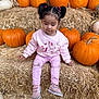 child, toddler, pink_clothing, pumpkins, hay_bales, fall, autumn, outdoor, cute, pigtails, shoes, sitting, seasonal, harvest, nature, playful, portrait, young_girl, casual, daylight