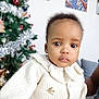 baby, child, portrait, sweater, white_clothing, indoor, christmas_tree, decoration, holiday, blurred_background, face, cute, young_child, knitwear, person, expression, closeup, cozy, festive, holiday_season