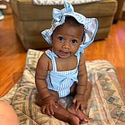 Ta Layah joined the competition — help win amazing prizes! baby, child, indoor, quilt, couch, floor, hat, blue, striped_clothing, smile, sitting, curious, infant, skin, wide_eyes, patterned, comfortable, cute, young, portrait