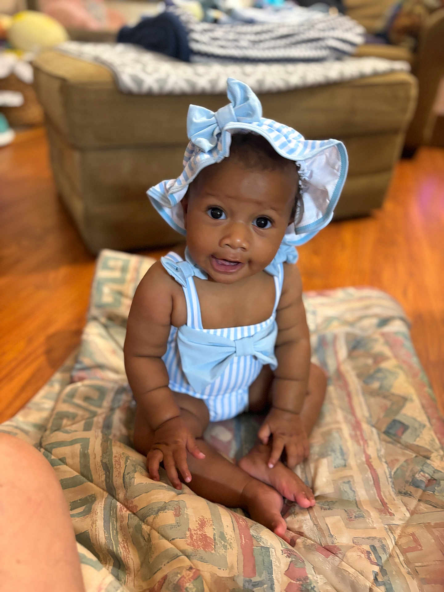 Ta Layah joined the competition — help win amazing prizes! baby, child, indoor, quilt, couch, floor, hat, blue, striped_clothing, smile, sitting, curious, infant, skin, wide_eyes, patterned, comfortable, cute, young, portrait