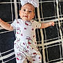 baby, infant, child, headband, bow, hello_kitty, patterned_clothing, white_clothing, pink_bows, blanket, black_and_white, floor, lying_down, cute, smiling, portrait, indoor, human, face, happy