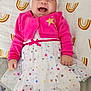 baby, infant, smiling, laughing, pink_cardigan, white_tutu, headband, bow, stars, patterned_blanket, rainbow_pattern, lying_down, cute, happy, child, toddler, clothing, fabric, indoors, portrait