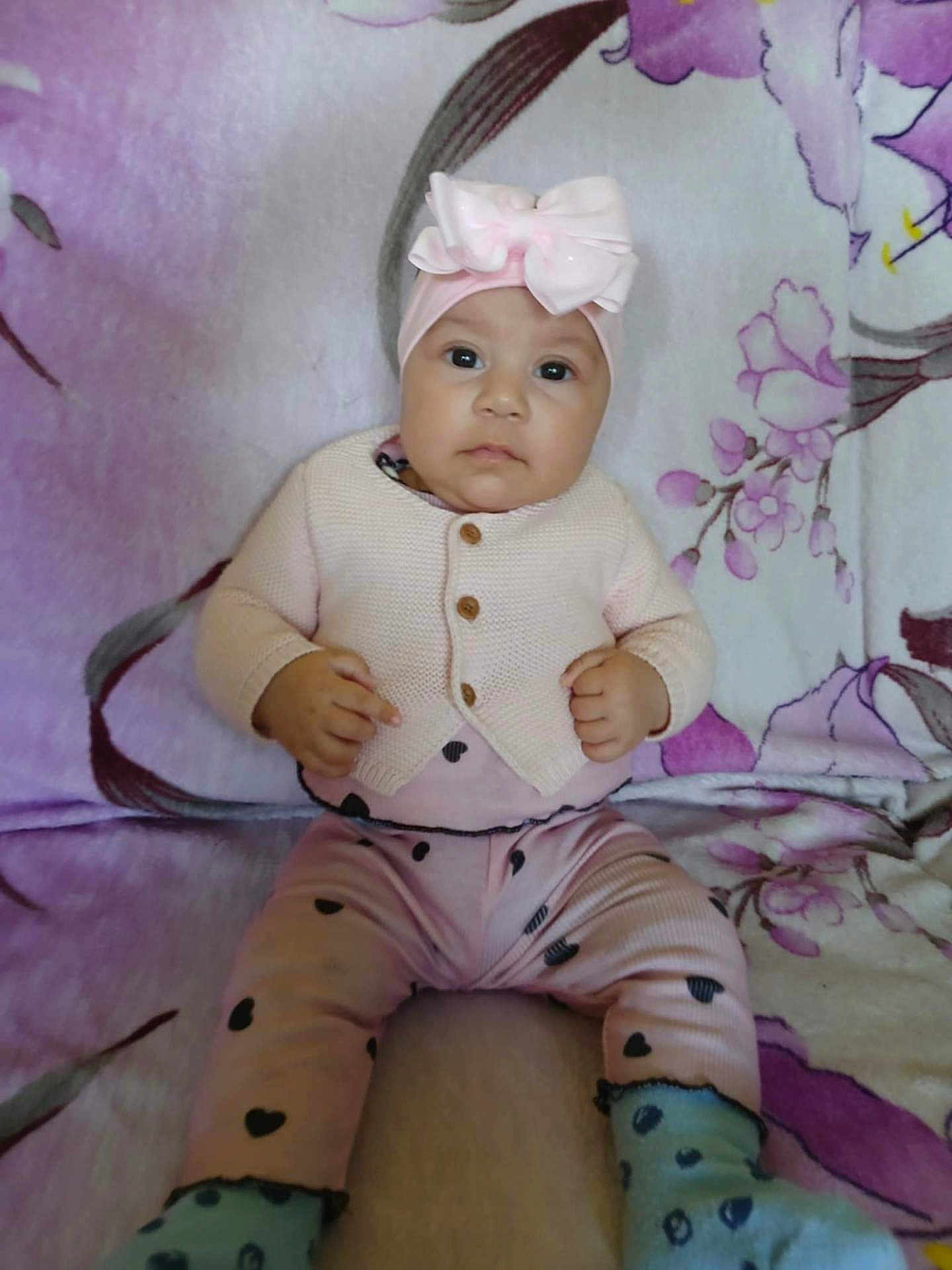 Seyda Melody is registered to the contest to win money with this photo: baby, blanket, bow, child, cozy, cute, expression, face, feet, floral_pattern, hands, headband, heart_pattern, indoor, infant, person, pink_clothing, portrait, sitting, socks
