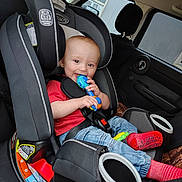 Ryder joined the competition — help win amazing prizes! baby, car_seat, toy, red_shirt, blue_jeans, red_socks, child, infant, car_interior, seatbelt, smiling, happy, cute, safety, window, rain, headrest, seat, toddler, person