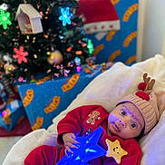 Ohena a rejoint le concours — aidez-le/la à gagner de superbes lots ! baby, child, christmas_tree, holiday, gift, present, red_clothing, reindeer_hat, star_wand, glowing_toy, blanket, indoor, festive, cute, smiling_star, decorations, ornament, christmas, holiday_lighting, cozy