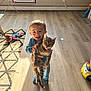 Hunter is registered to the contest to win money with this photo: toddler, cat, child, pajamas, toy, floor, rug, air_conditioner, window, smiling, indoor, playtime, animal, pet, happy, person, furniture, light, home, cute