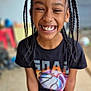 child, smiling, braided_hair, black_tshirt, basketball_graphic, indoor, tiled_floor, holding_object, joyful, happy, portrait, person, casual_clothing, young, standing, closeup, face, teeth, expression, playful