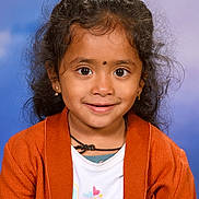 Nila participe au concours pour gagner de l'argent avec cette photo : child, girl, portrait, smile, curly_hair, orange_cardigan, earrings, necklace, colorful_shirt, hearts_pattern, studio_background, happy, cute, innocent, closeup, person, fashion, young, face, eyes