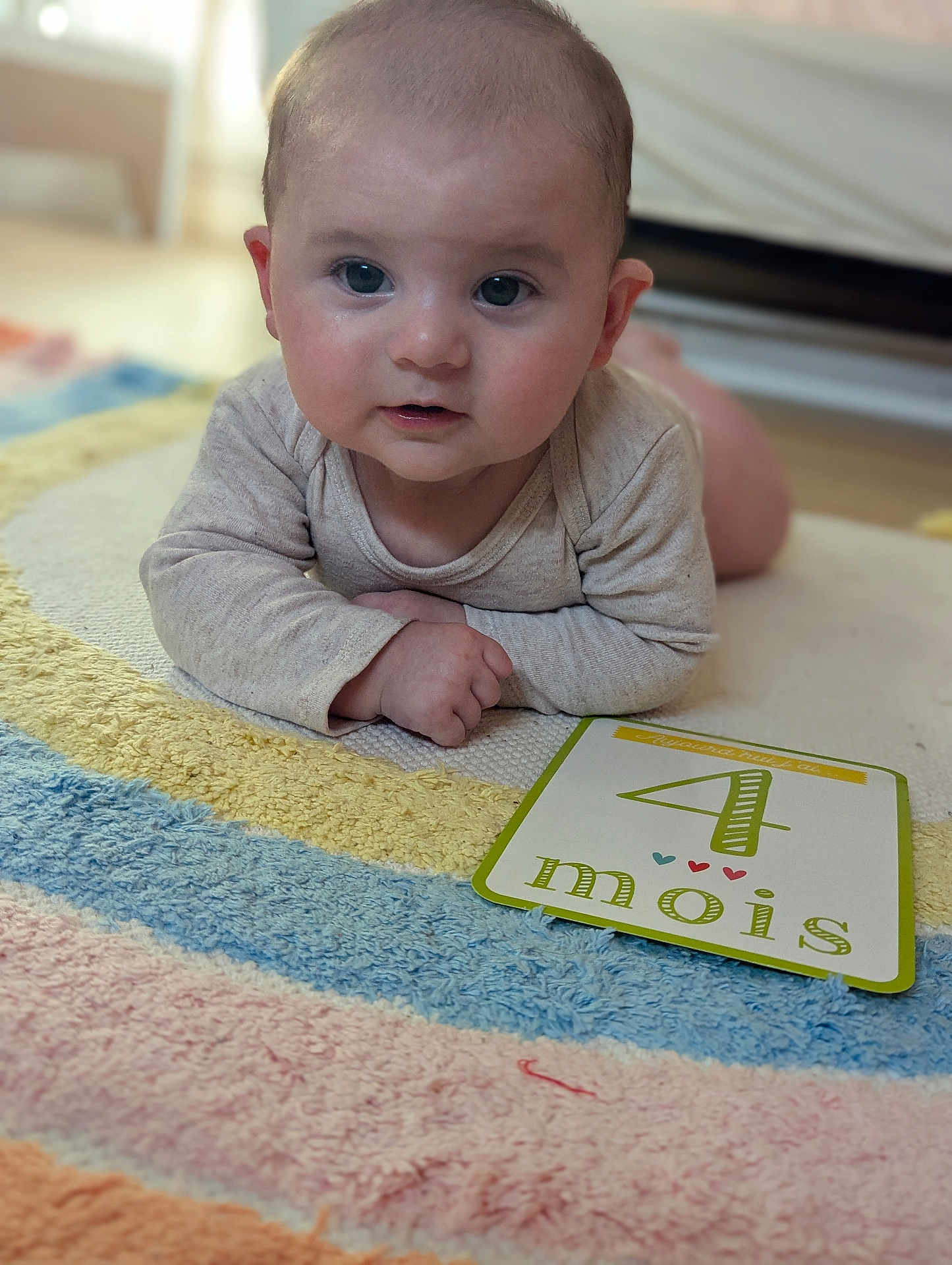 Ella a rejoint le concours — aidez-le/la à gagner de superbes lots ! baby, infant, milestone_card, colorful_rug, indoor, cute, portrait, child, lying_down, soft_lighting, four_months, closeup, face, hands, floor, expression, young_child, home, cozy, toddler