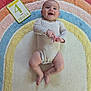 Ella participe au concours pour gagner de l'argent avec cette photo : baby, infant, smiling, onesie, milestone_card, colorful_rug, rainbow_pattern, floor, wooden_floor, happy, child, person, cute, indoor, playtime, laying_down, skin, hands, feet, expression