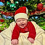 baby, child, christmas, holiday, festive, smiling, happy, red_hat, blanket, christmas_tree, ornaments, decorations, santa_hat, holiday_clothing, infant, celebration, joyful, seasonal, indoors, cute