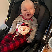 John is registered to the contest to win money with this photo: baby, smiling, infant, stroller, clothing, pajamas, indoor, child, seat, happy, person, cute, red, black, plaid, face, head, babywear, cozy, holiday