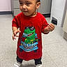toddler, child, standing, portrait, smiling, red_shirt, dinosaur_shirt, sneakers, indoor, clinic, cabinet, floor_tiles, trash_bin, hands, short_hair, cute, casual_clothing, full_body, photograph, playful