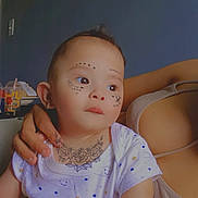 Eliel is registered to the contest to win money with this photo: baby, child, tattoos, face, neck, clothing, pattern, stars, clouds, hand, adult, arm, bracelet, earring, portrait, indoor, person, cute, gaze, holding