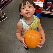 Angelrey is registered to the contest to win money with this photo: child, ball, store, snacks, shelf, floor, drink, beverage, orange, tank_top, short_hair, curious, shopping, aisle, person, indoor, colorful, retail, food, young