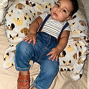 Lucas joined the competition — help win amazing prizes! baby, child, infant, face, person, clothing, striped_shirt, denim, overalls, suspenders, brown_shoes, plush_pillow, dog_pattern, bed, blanket, cute, indoor, portrait, relaxed, fashion