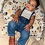 baby, child, infant, face, person, clothing, striped_shirt, denim, overalls, suspenders, brown_shoes, plush_pillow, dog_pattern, bed, blanket, cute, indoor, portrait, relaxed, fashion