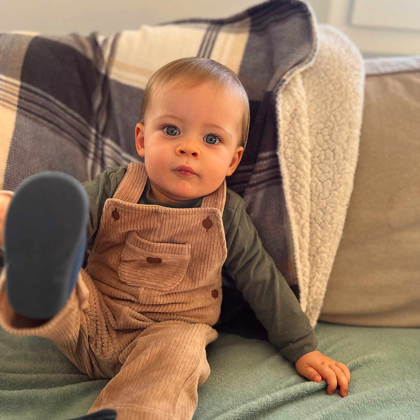 Côme a rejoint le concours — aidez-le/la à gagner de superbes lots ! blue_eyes, child, corduroy, couch, cozy, curious_expression, cushion, footwear, green_shirt, hand, indoor, leg, overalls, plaid_blanket, portrait, sitting, soft_fabric, toddler, window, young_child