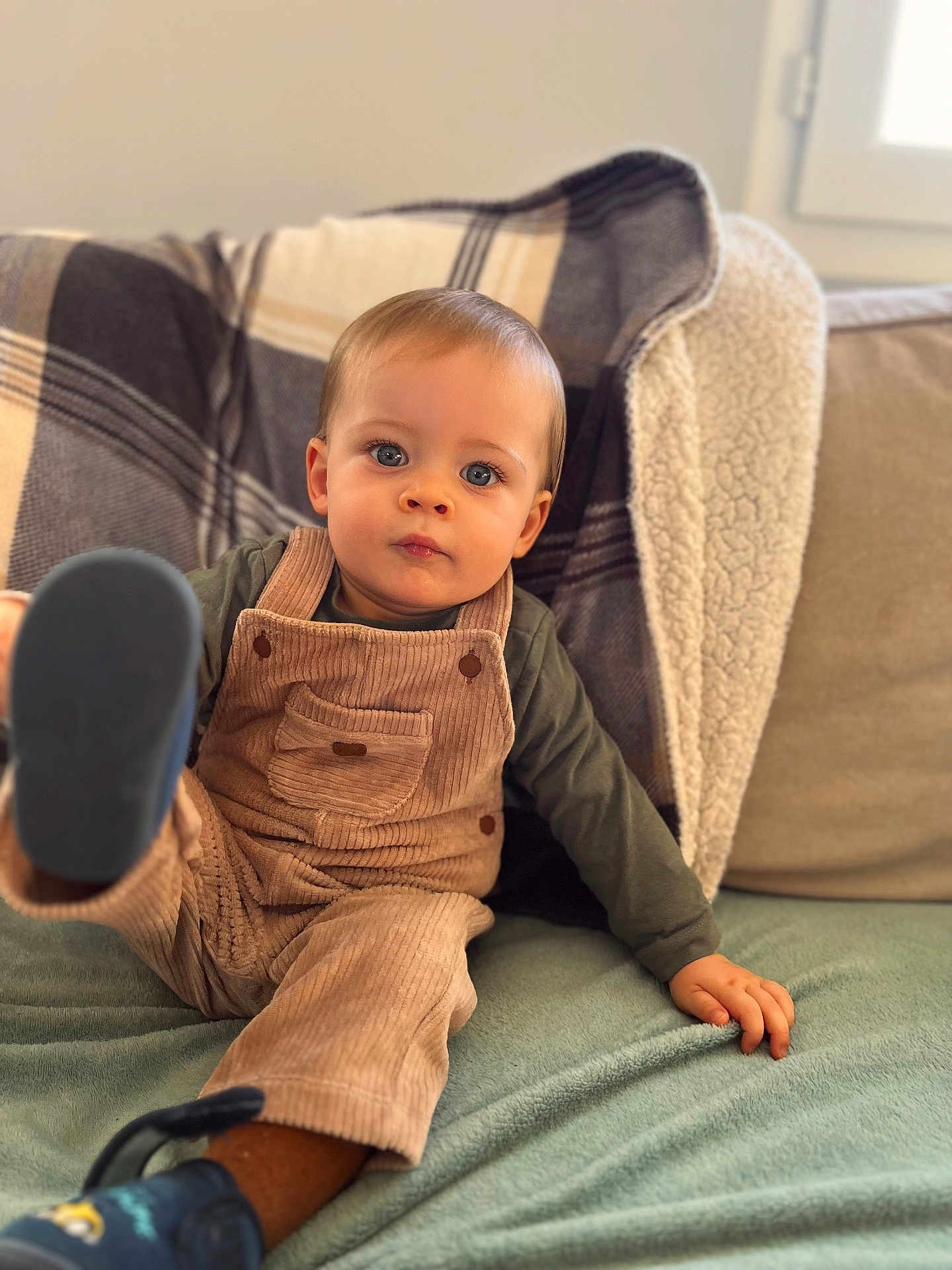 Côme a rejoint le concours — aidez-le/la à gagner de superbes lots ! toddler, child, overalls, corduroy, green_shirt, blue_eyes, plaid_blanket, couch, cushion, indoor, window, soft_fabric, footwear, curious_expression, sitting, hand, leg, cozy, portrait, young_child