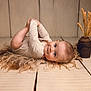 baby, infant, child, blue_eyes, holding_feet, wooden_floor, vase, dried_wheat, rustic, soft_texture, curious_expression, natural_light, cozy, floorboards, portrait, cute, laying_down, indoors, warm_colors, smiling