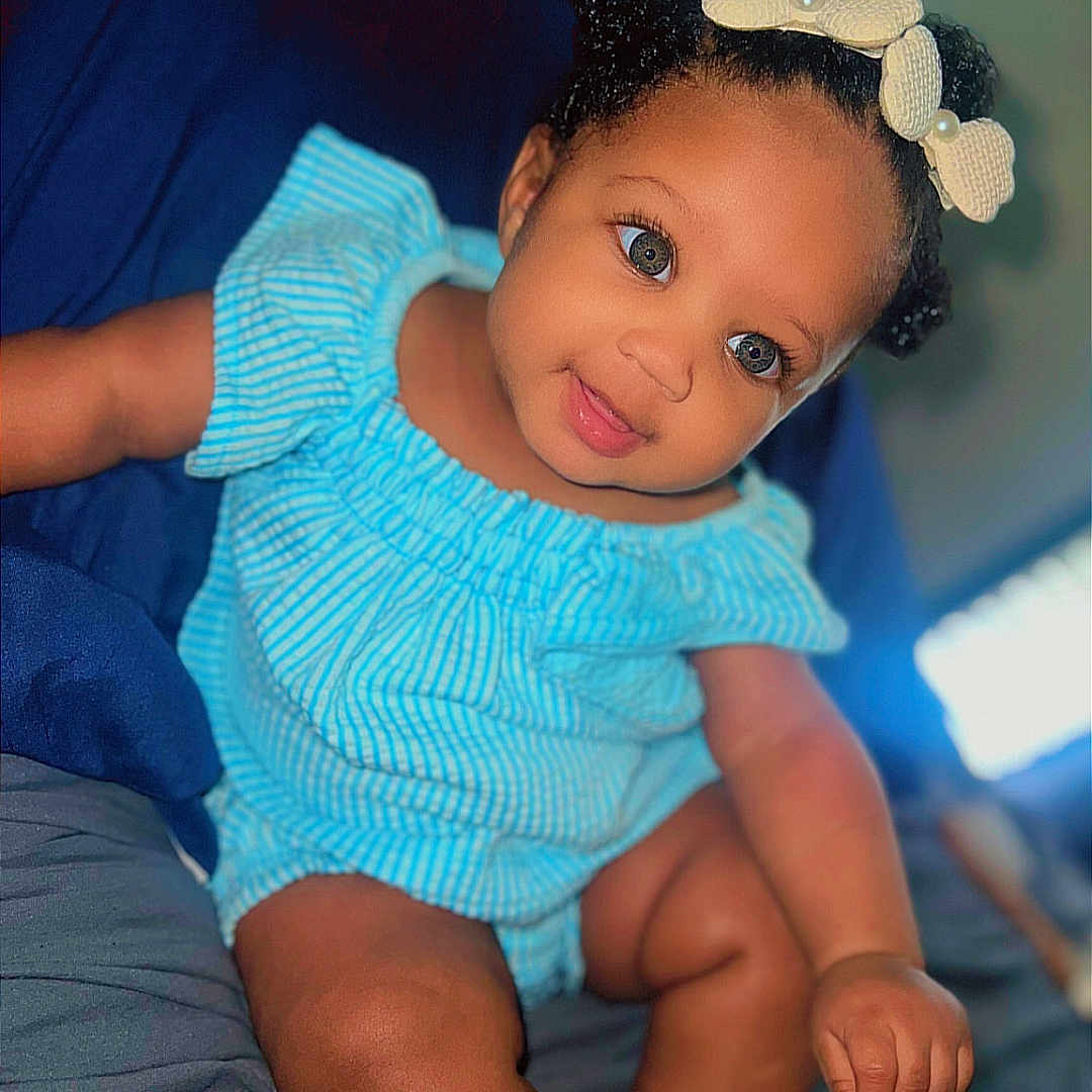 Mi'Aila joined the competition — help win amazing prizes! baby, bed, blue_outfit, bow, child, comfort, cute, eyes, face, foot, hand, happy, headband, indoors, infant, portrait, sitting, skin, smiling, young