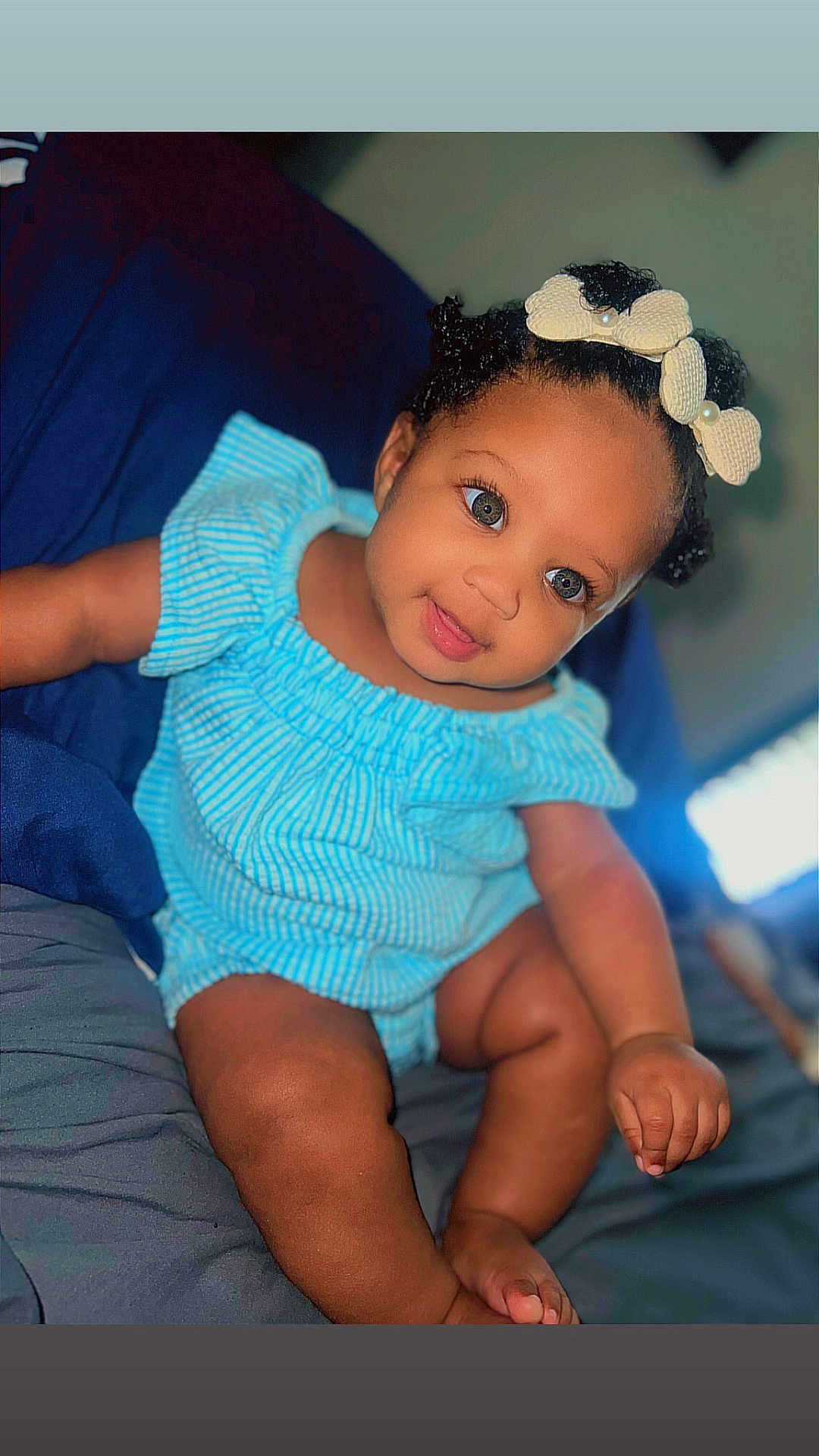 Mi'Aila joined the competition — help win amazing prizes! baby, child, infant, smiling, blue_outfit, bow, headband, sitting, bed, comfort, cute, skin, face, eyes, hand, foot, indoors, portrait, happy, young