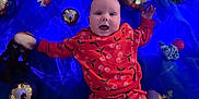 Bella-Rose is registered to the contest to win money with this photo: baby, blue_background, cherry_pattern, child, colorful, crocheted_toys, cute, fabric, happy, indoors, infant, joyful, lying_down, playful, portrait, red_clothing, silver_balls, smiling, soft_toys, young_child