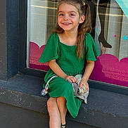 Syanna a rejoint le concours — aidez-le/la à gagner de superbes lots ! building, child, concrete, cute, daylight, girl, green_dress, hairclip, happy, outdoor, pacifier, person, portrait, reflection, sandals, sitting, smile, street, toy, window