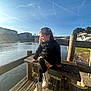 Syanna participe au concours pour gagner de l'argent avec cette photo : child, girl, smiling, bench, river, water, wood, sunlight, outdoor, sky, clouds, trees, building, bridge, jacket, boots, happy, nature, daylight, portrait