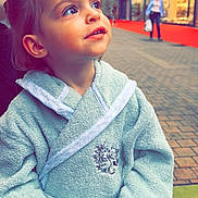 Syanna participe au concours pour gagner de l'argent avec cette photo : toddler, child, bathrobe, street, urban, sidewalk, building, shop, pavement, curious, looking_up, person, outdoor, daylight, casual, young_child, portrait, clothing, hand, face
