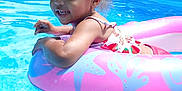 Sylvi is registered to the contest to win money with this photo: child, toddler, pool, water, inflatable_ring, pink, blue, summer, outdoor, sunny, trees, smiling, swimwear, curly_hair, recreation, fun, daylight, nature, playful, relaxation