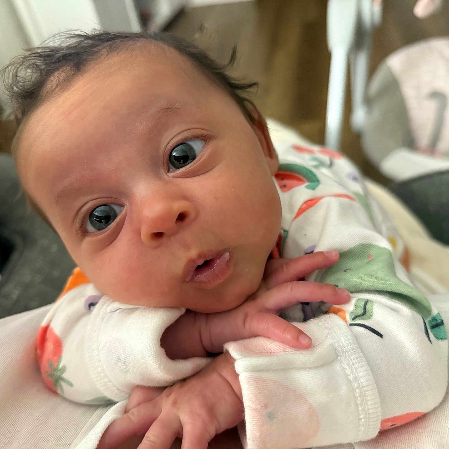 Meadow is registered to the contest to win money with this photo: baby, blurred_background, closeup, clothing, curious, cute, expression, eyes, face, fruit, hands, indoor, infant, newborn, onesie, pattern, person, resting, skin, soft_surface