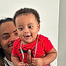 baby, man, child, smile, red_shirt, chain, dreadlocks, holding, happy, indoor, portrait, person, cute, affection, family, skin, face, hand, casual_clothing, joy