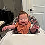 baby, high_chair, bib, smiling, happy, indoor, child, person, hair, face, arm, table, door, furniture, room, clothing, expression, infant, seat, background
