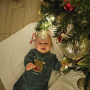 Livio a rejoint le concours — aidez-le/la à gagner de superbes lots ! baby, child, christmas_tree, ornaments, candy_cane, blanket, floor, holiday, smile, reindeer_outfit, festive, decorations, indoor, infant, cute, cozy, lights, greenery, happy, celebration
