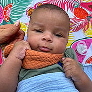 Camil is registered to the contest to win money with this photo: baby, infant, blanket, hand, pacifier, colorful, fruit_pattern, tropical, orange_cloth, green_shirt, face, cheeks, lying_down, outdoor, grass, closeup, expression, skin, person, child