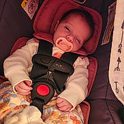Lilith is registered to the contest to win money with this photo: baby, infant, pacifier, car_seat, safety_harness, buckle, blanket, floral_pattern, onesie, sleepy, hand, face, head_support, warning_label, fabric, pink, close_up, portrait, booties, cozy