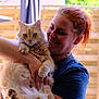 affection, animal, casual_clothing, cat, cute, daylight, domestic_animal, fence, fluffy_cat, ginger_cat, happy, holding, nature, outdoor, person, pet, portrait, red_hair, smiling, sunlight