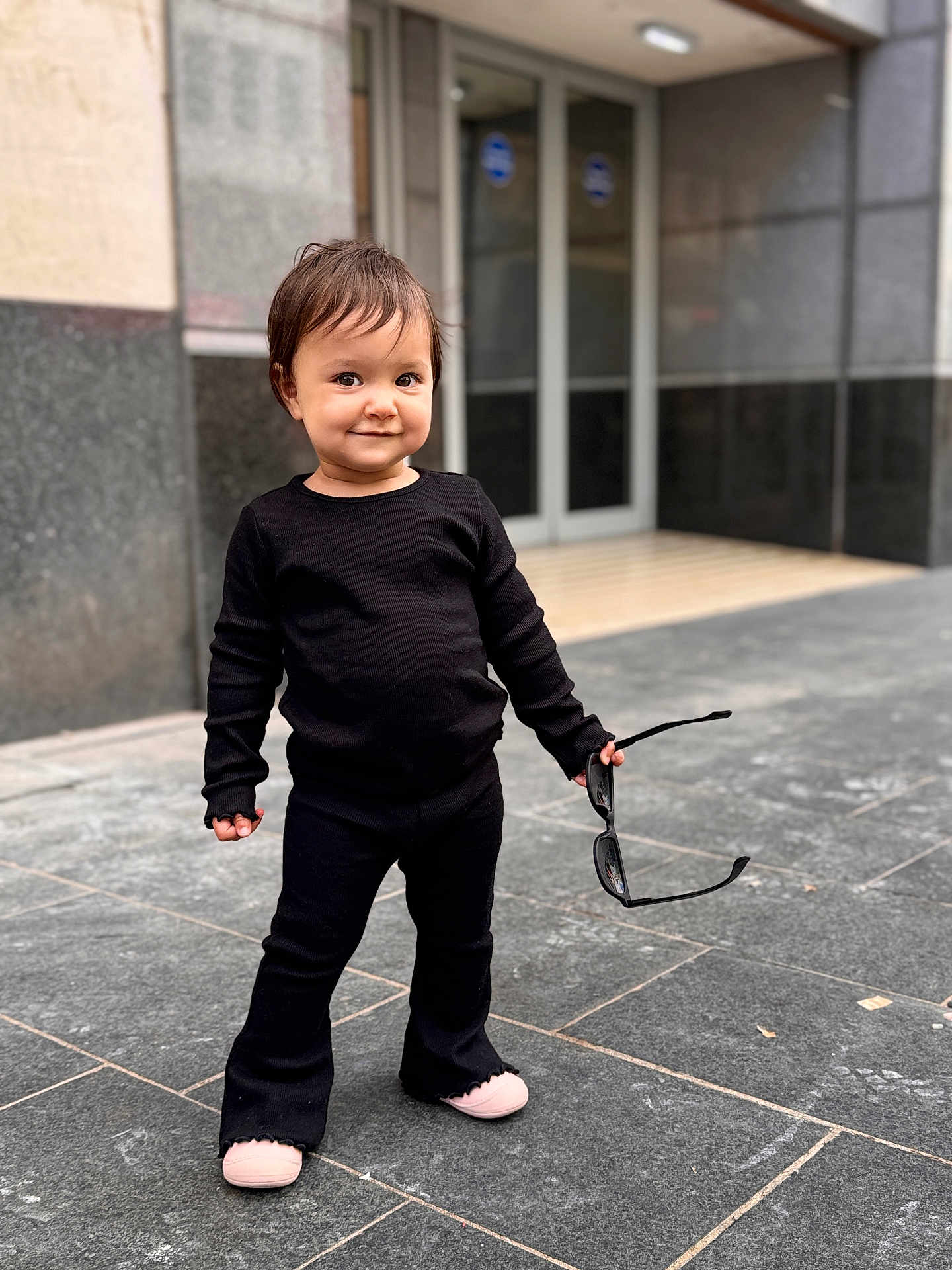 Naomi joined the competition — help win amazing prizes! toddler, child, black_clothing, sunglasses, sidewalk, urban, street, standing, smiling, face, person, footwear, cute, confident, outdoor, casual, young_child, happy, fashion, playful