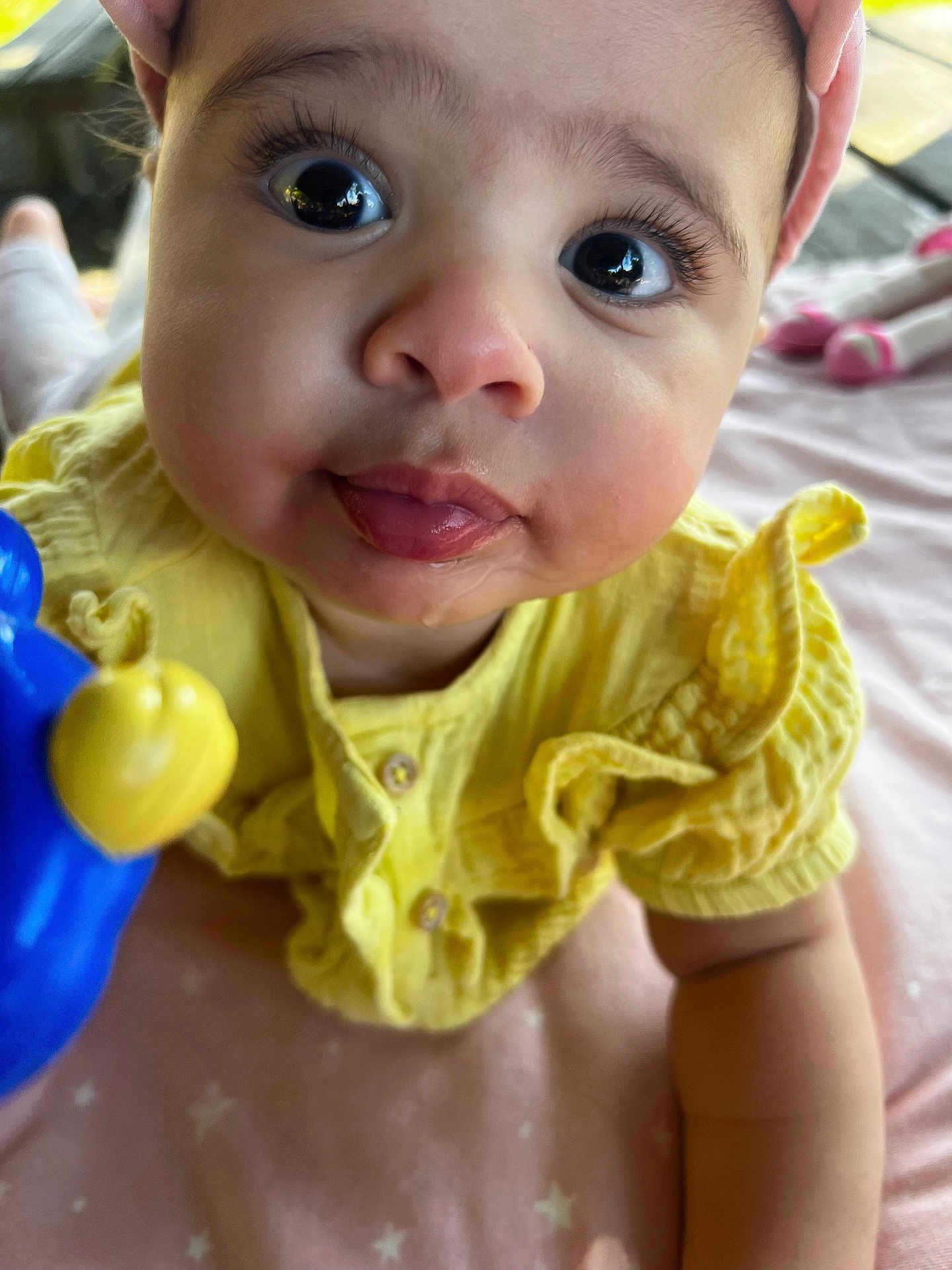Niema a rejoint le concours — aidez-le/la à gagner de superbes lots ! baby, child, chubby_cheeks, close_up, curious_eyes, cute, doll, face, hand, indoors, infant, pink_blanket, playful, portrait, smiling, soft_lighting, tongue_out, toy, yellow_clothing, young_child