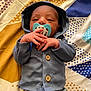 baby, newborn, pacifier, blue_hoodie, striped_pants, hands, face, lying_down, blanket, patterned, cute, infant, clothing, sleepy, indoors, portrait, small_hands, buttoned_clothes, baby_girl, baby_boy